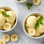Cottage cheese banana ice cream scoops in white bowls with fresh banana garnish