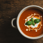 Homemade 3 ingredient tomato soup in white bowl with cream swirl and basil garnish